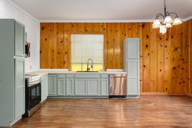 kitchen featuring wood walls, sink, stainless steel appliances, and hanging light fixtures