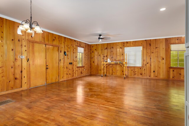 unfurnished living room with hardwood / wood-style floors, ceiling fan with notable chandelier, and crown molding