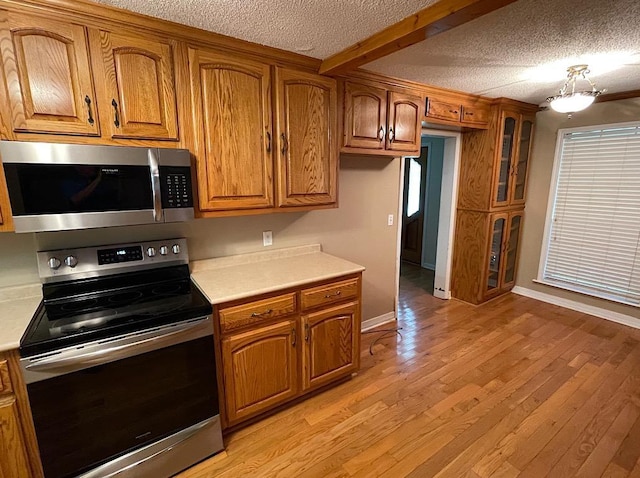 kitchen featuring light wood-type flooring, a textured ceiling, and appliances with stainless steel finishes