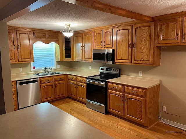 kitchen featuring sink, hanging light fixtures, light hardwood / wood-style flooring, beam ceiling, and stainless steel appliances