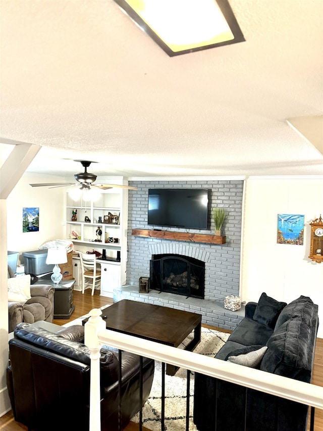 living room with built in shelves, ceiling fan, a fireplace, and wood-type flooring