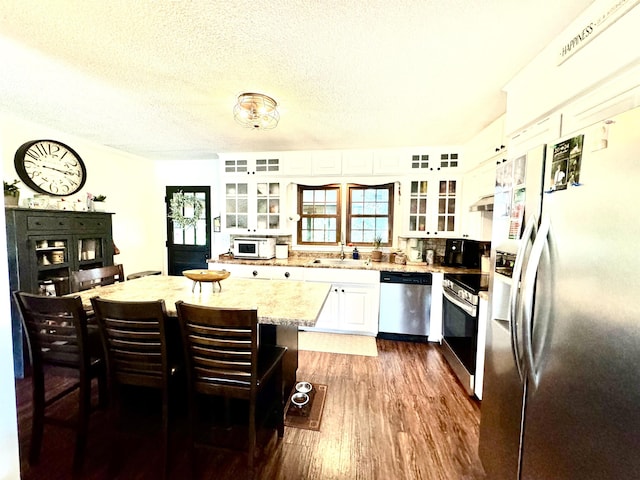 kitchen featuring white cabinetry, light stone countertops, dark hardwood / wood-style floors, a kitchen bar, and appliances with stainless steel finishes