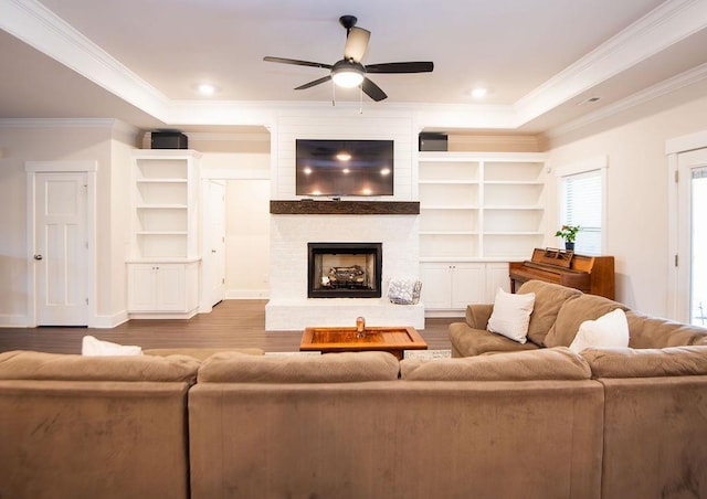 living room featuring hardwood / wood-style floors, a raised ceiling, ceiling fan, ornamental molding, and a fireplace