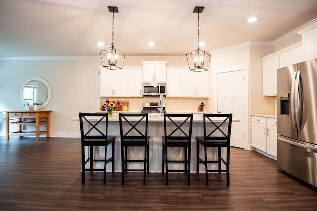 kitchen with white cabinets, appliances with stainless steel finishes, decorative light fixtures, and an island with sink