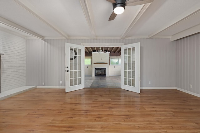  - unfurnished living room with a fireplace, ceiling fan, light wood-type flooring, beamed ceiling, and french doors