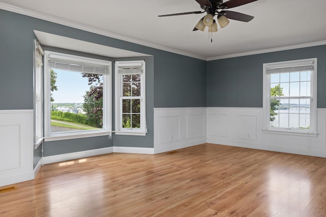  - spare room with wainscoting, ornamental molding, light wood-type flooring, and a ceiling fan