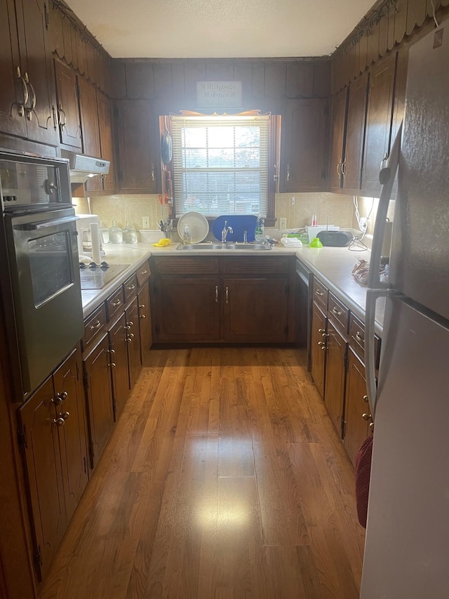 kitchen with sink, white refrigerator, black electric stovetop, stainless steel oven, and light hardwood / wood-style floors