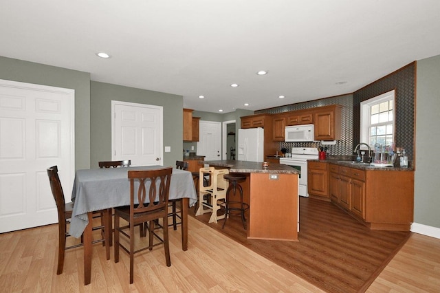 kitchen with a breakfast bar, a kitchen island, white appliances, and light hardwood / wood-style flooring