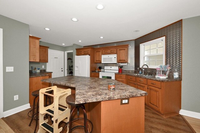 kitchen featuring a breakfast bar, white appliances, dark wood-type flooring, sink, and a center island