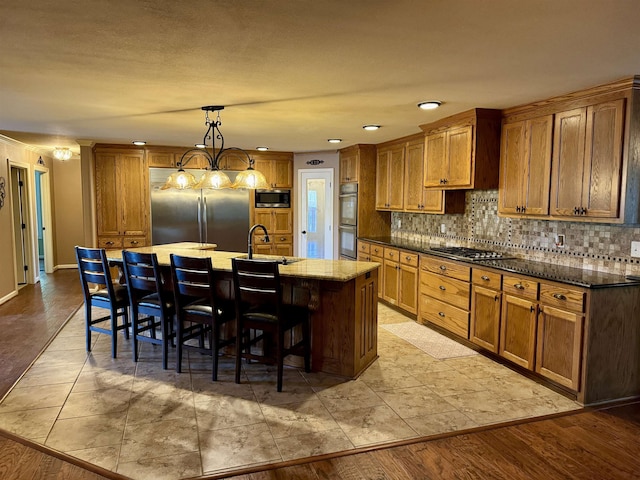 kitchen with sink, pendant lighting, built in appliances, a center island with sink, and a breakfast bar area