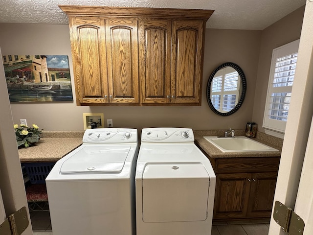 laundry area featuring a sink, cabinet space, washing machine and clothes dryer, a textured ceiling, and light tile patterned flooring