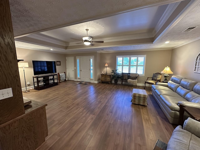 living room with wood finished floors, ornamental molding, a ceiling fan, a raised ceiling, and baseboards