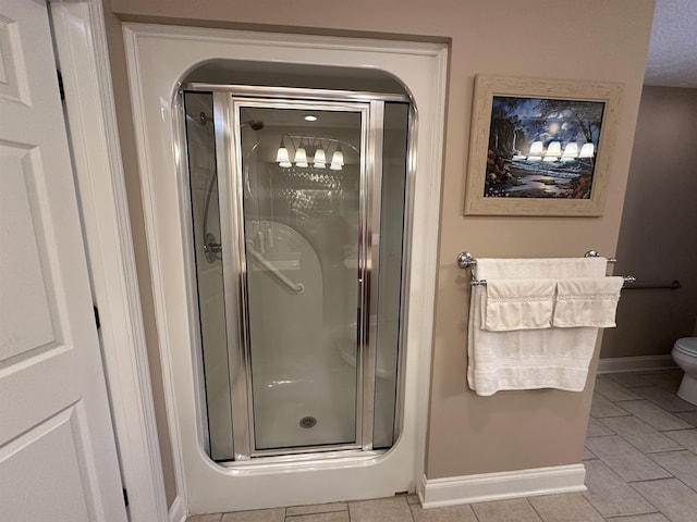 bathroom featuring toilet, baseboards, and a shower stall
