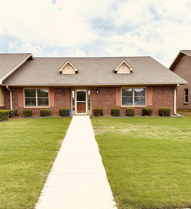 ranch-style home featuring a shingled roof, brick siding, and a front yard