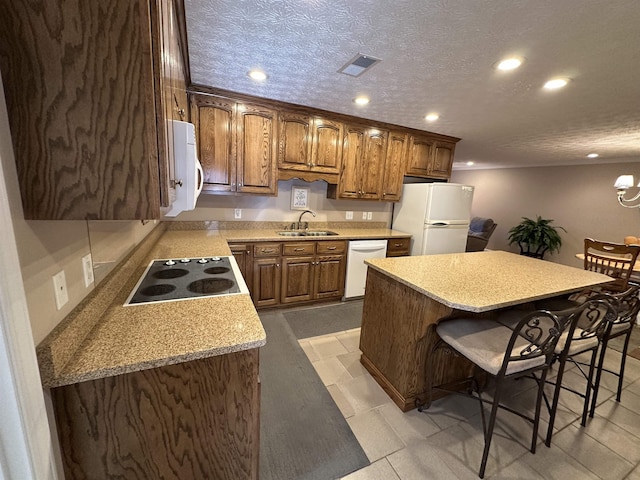 kitchen with a breakfast bar area, a sink, visible vents, white appliances, and recessed lighting