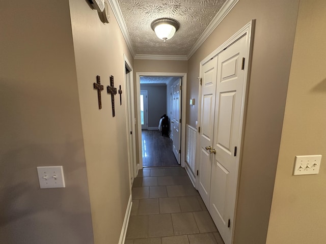 hall with crown molding, a textured ceiling, dark tile patterned floors, and baseboards