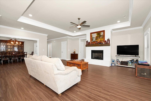 living room featuring a tray ceiling, crown molding, dark wood-type flooring, and ceiling fan with notable chandelier