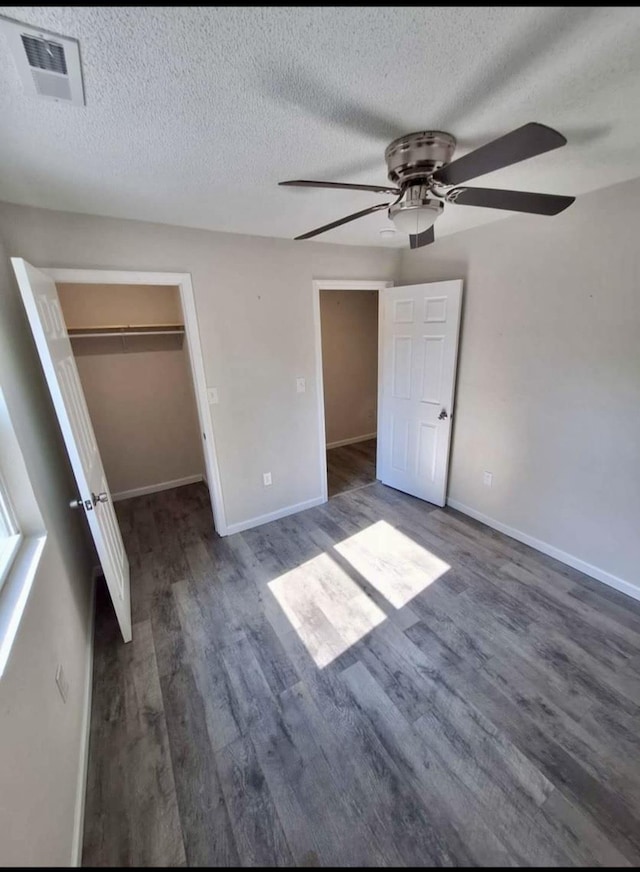 unfurnished bedroom featuring a walk in closet, ceiling fan, dark hardwood / wood-style floors, a textured ceiling, and a closet