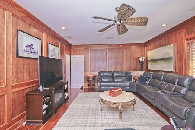 living room featuring crown molding, a ceiling fan, wood walls, and dark wood-type flooring