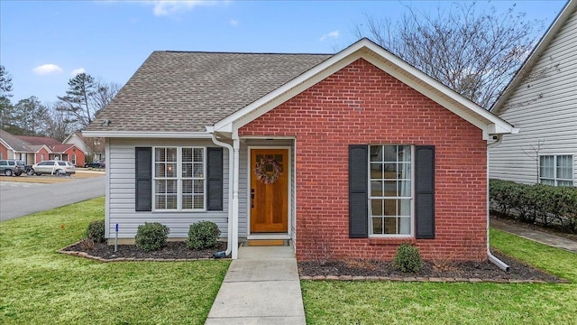 view of front of house with a front lawn, a shingled roof, and brick siding