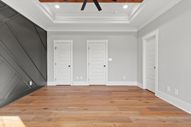 unfurnished bedroom with ornamental molding, a raised ceiling, two closets, ceiling fan, and light hardwood / wood-style floors