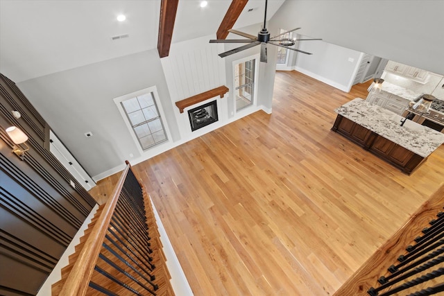 unfurnished living room with light hardwood / wood-style flooring, lofted ceiling with beams, and ceiling fan