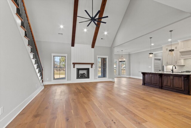 unfurnished living room with sink, high vaulted ceiling, light wood-type flooring, beam ceiling, and ceiling fan with notable chandelier