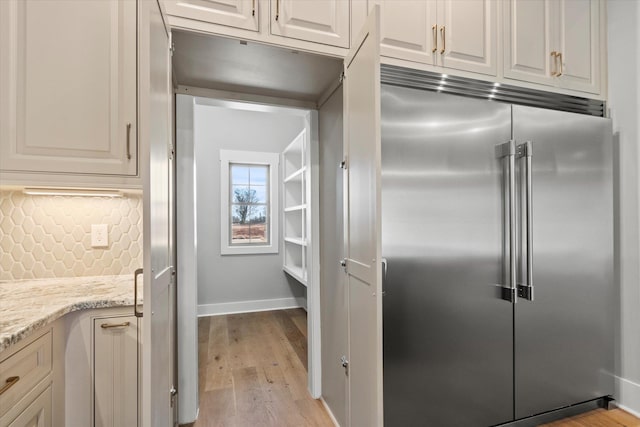 kitchen featuring light stone counters, built in fridge, baseboards, light wood-style floors, and decorative backsplash