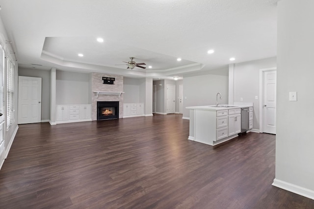  - unfurnished living room featuring a tray ceiling, a ceiling fan, dark wood-style flooring, recessed lighting, and a stone fireplace
