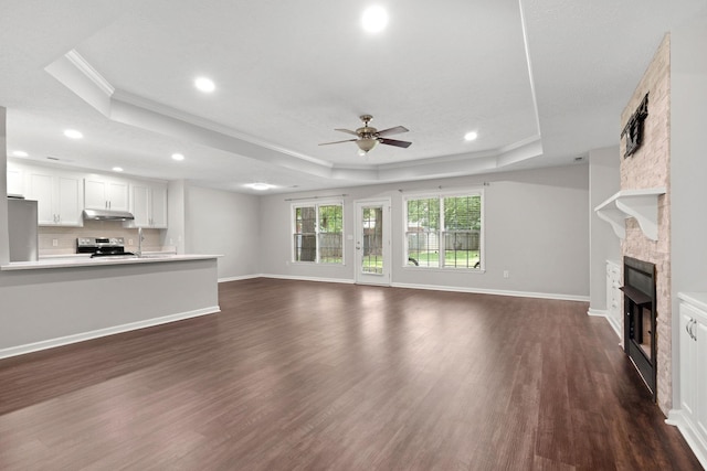  - unfurnished living room with a raised ceiling, crown molding, a ceiling fan, a fireplace, and dark wood finished floors