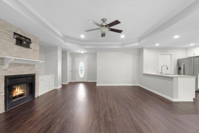  - unfurnished living room featuring a raised ceiling, ceiling fan, dark wood-style flooring, crown molding, and a fireplace