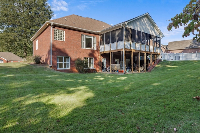 rear view of house with a sunroom, fence, brick siding, and a yard