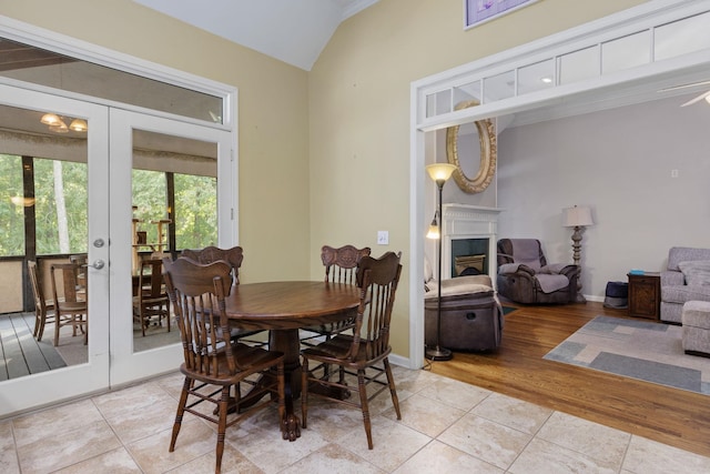 dining room featuring baseboards, vaulted ceiling, french doors, a fireplace, and light tile patterned flooring