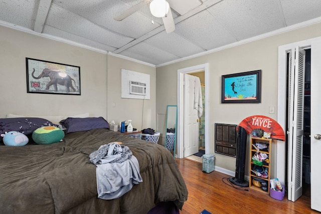 bedroom featuring ornamental molding, ensuite bathroom, a ceiling fan, a wall mounted AC, and wood finished floors