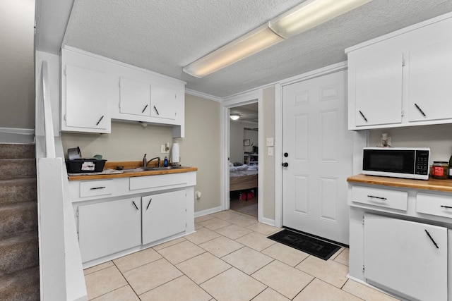 kitchen featuring white microwave, light tile patterned floors, white cabinets, a textured ceiling, and a sink