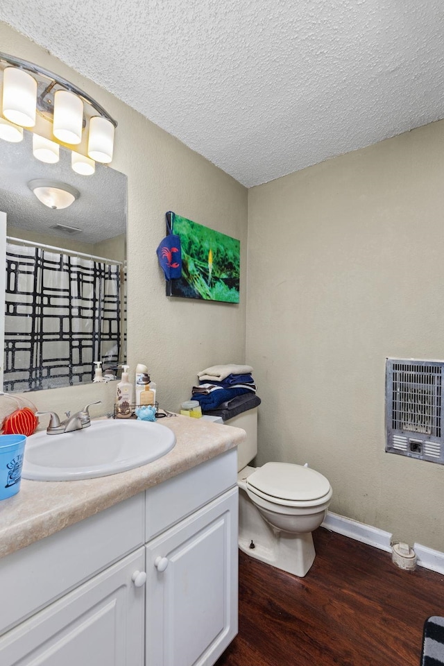 bathroom featuring toilet, heating unit, a textured ceiling, wood finished floors, and vanity