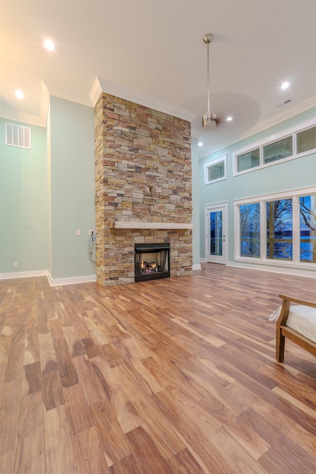 unfurnished living room with crown molding, a stone fireplace, and light wood-type flooring