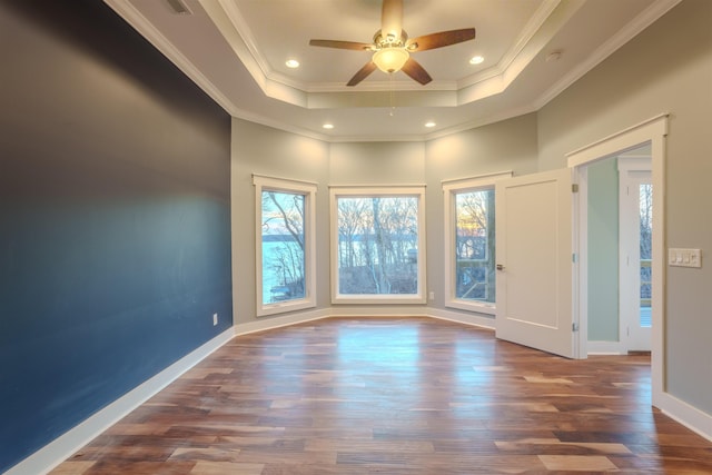 empty room with dark hardwood / wood-style floors, a tray ceiling, crown molding, and a wealth of natural light