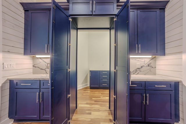 kitchen with blue cabinetry, light stone countertops, and light wood-type flooring