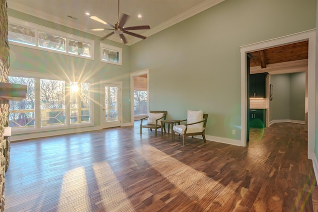 living area with dark hardwood / wood-style floors, a towering ceiling, ceiling fan, crown molding, and beam ceiling