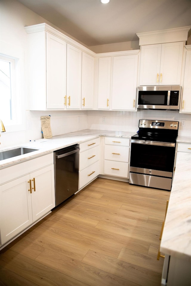 kitchen with sink, white cabinetry, stainless steel appliances, and light hardwood / wood-style flooring