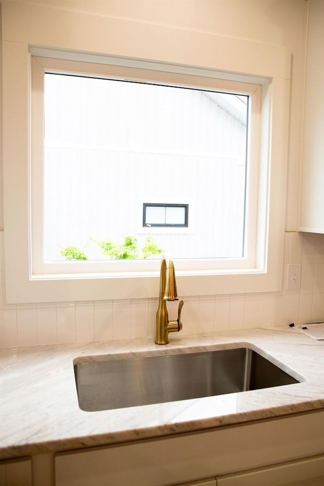 interior details featuring backsplash, light stone counters, and sink