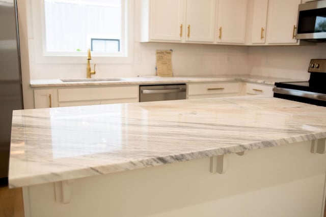 kitchen with white cabinets, light stone counters, sink, and stainless steel appliances