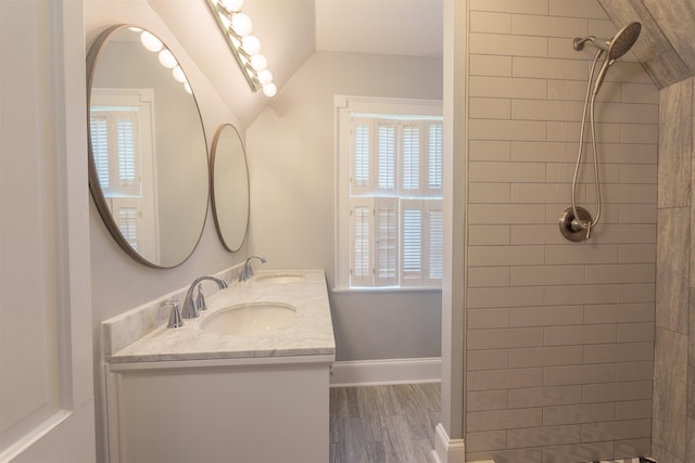 bathroom featuring plenty of natural light, wood finished floors, a tile shower, baseboards, and lofted ceiling