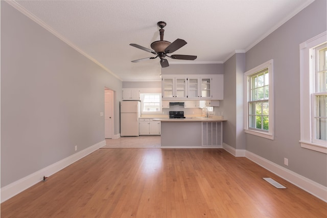 unfurnished living room with a sink, ornamental molding, light wood-style flooring, ceiling fan, and baseboards