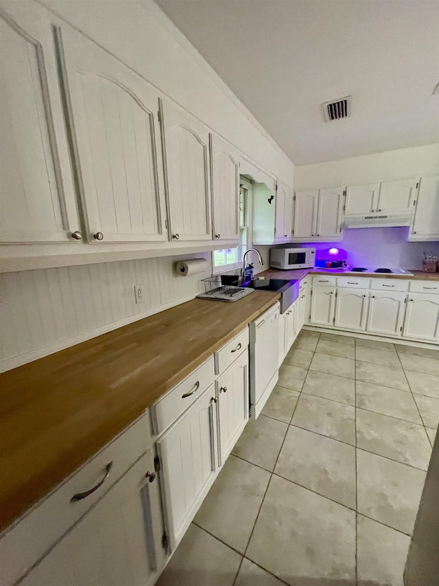  - kitchen featuring white appliances, butcher block counters, under cabinet range hood, light tile patterned floors, and white cabinetry