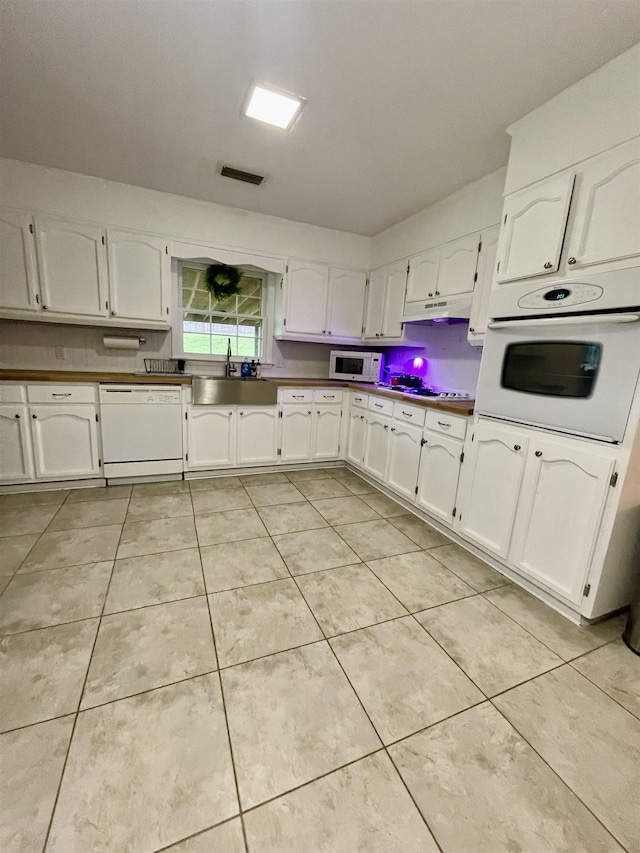  - kitchen featuring white appliances, white cabinetry, under cabinet range hood, and light tile patterned floors