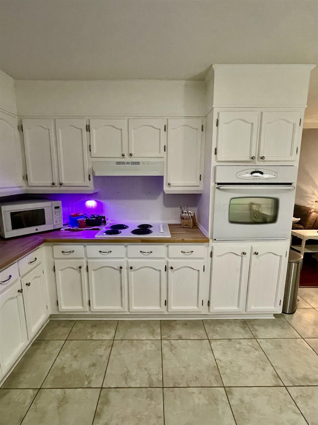  - kitchen featuring white appliances, under cabinet range hood, light tile patterned floors, and white cabinetry