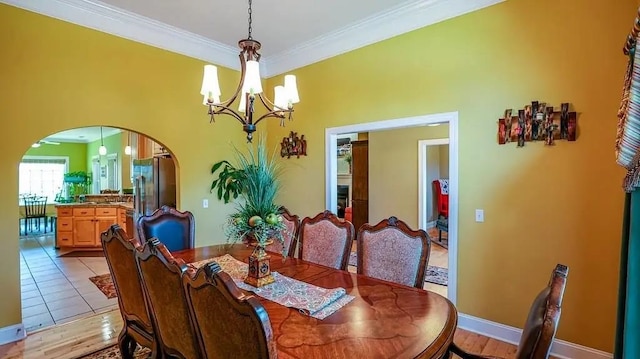 dining room featuring arched walkways, light tile patterned flooring, a notable chandelier, baseboards, and crown molding