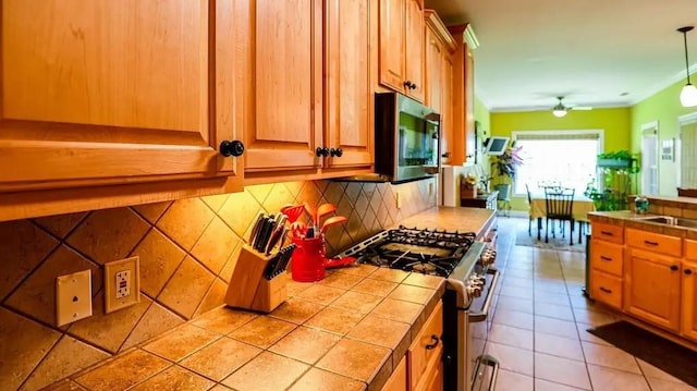 kitchen with stainless steel appliances, a sink, backsplash, tile counters, and decorative light fixtures